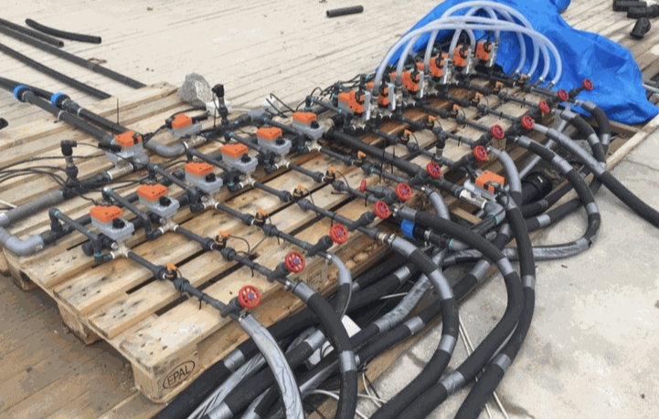 Valve manifold with orange valve actuators, red manual valves and black hoses on a wooden pallet