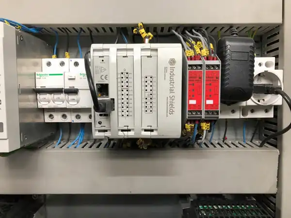 M-Duino PLC with two I/O zones on a DIN rail in the machine cabinet, next to two safety relay units and circuit breakers