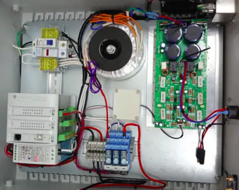 Inside the control cabinet: the Industrial Shields PLC at the bottom left, a toroidal transformer, interface relays and an electronic board with large capacitors